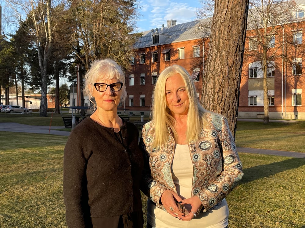 Två personer i halvfigur stående i en park i höstsol.