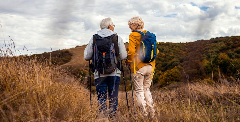 Två personer vandrar med ryggsäckar på en stig i ett öppet landskap.