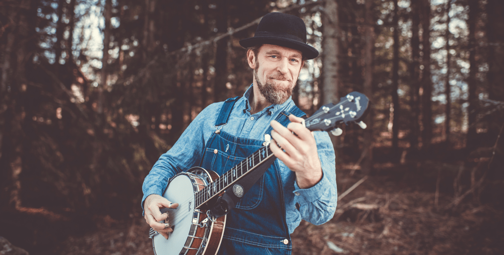 En man i overall som spelar gitarr i skogen.