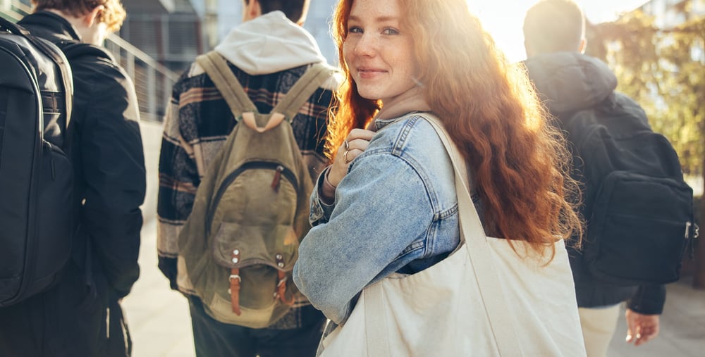 Female student glancing back while going for a class in college. Girl walking with friends going for class in high school.