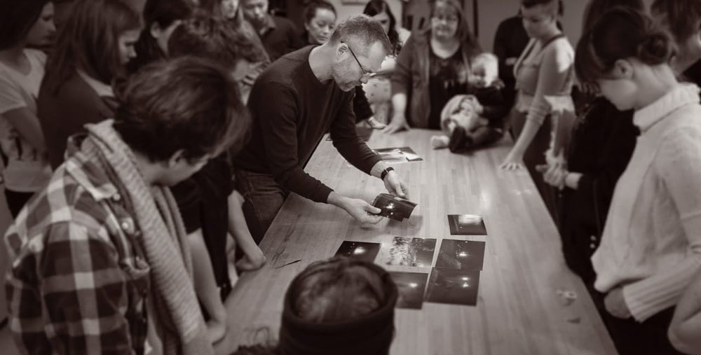 Människor står samlade runt ett bord där det visas fotografier