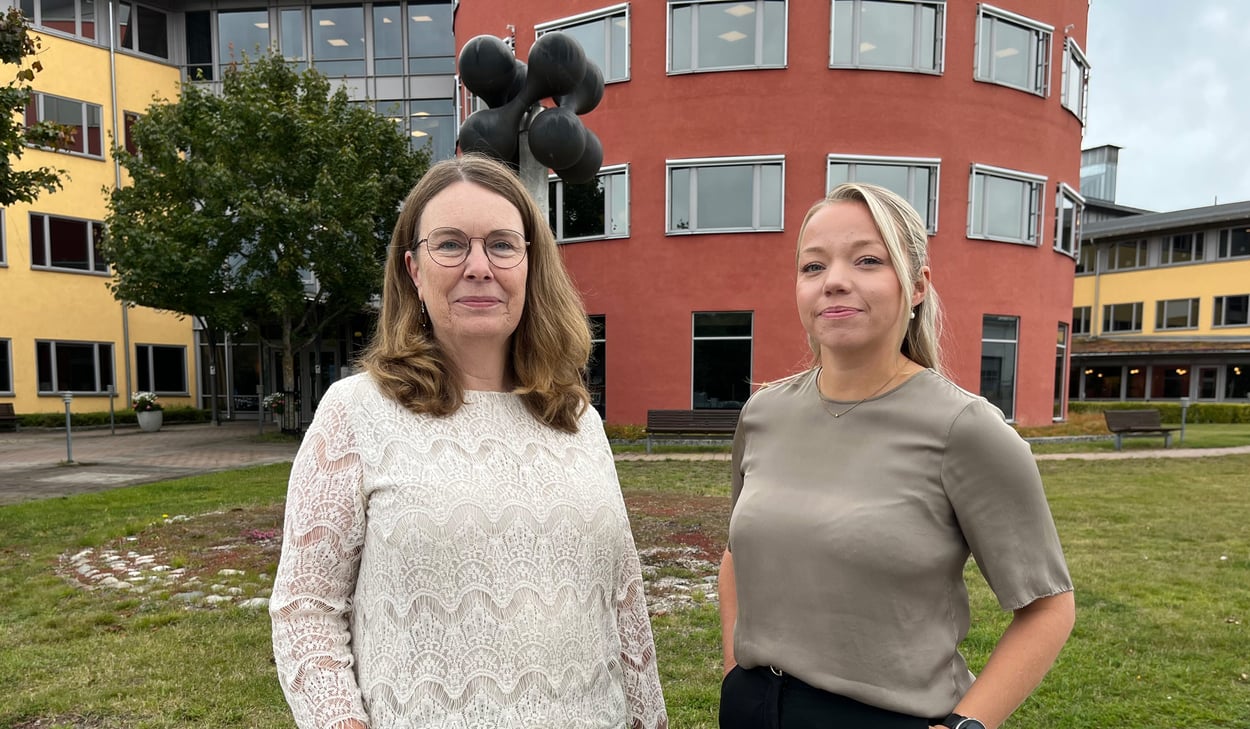 Två kvinnor i halvfigur framför en stor byggnad.