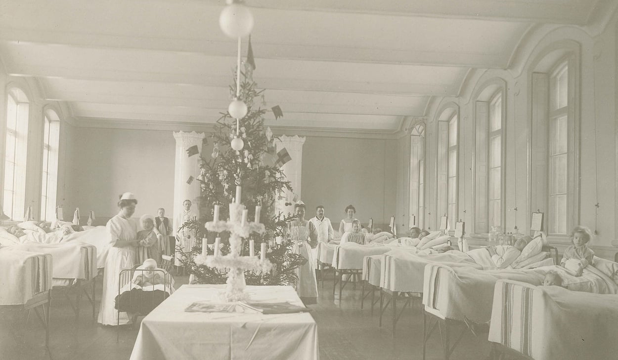 Svart-vit bild med en ny sjukhussal från 1900-talet. Dekorerad med julgran, barn i sängar och vårdpersonal i rummet