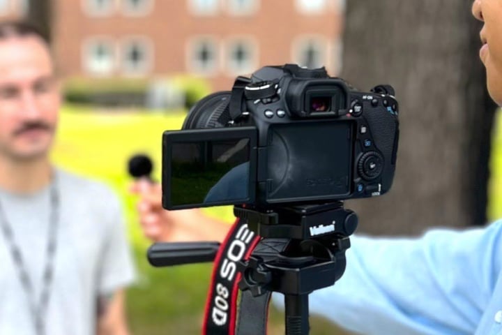 En person framför en filmkamera och en person bakom kameran. 