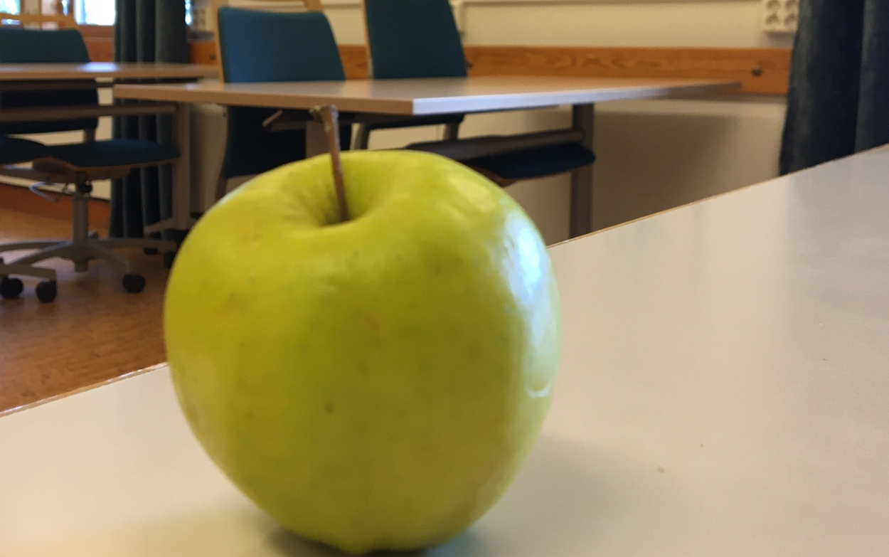 Ett gr&ouml;nt &auml;pple som ligger p&aring; en vit b&auml;nkskiva.