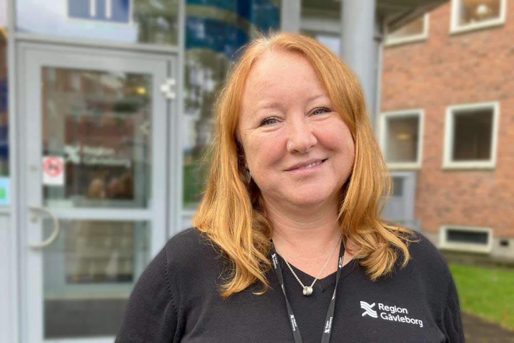 Porträtt av en person i arbetskläder med Region Gävleborgs logotyp, utomhus vid en byggnadsentré.