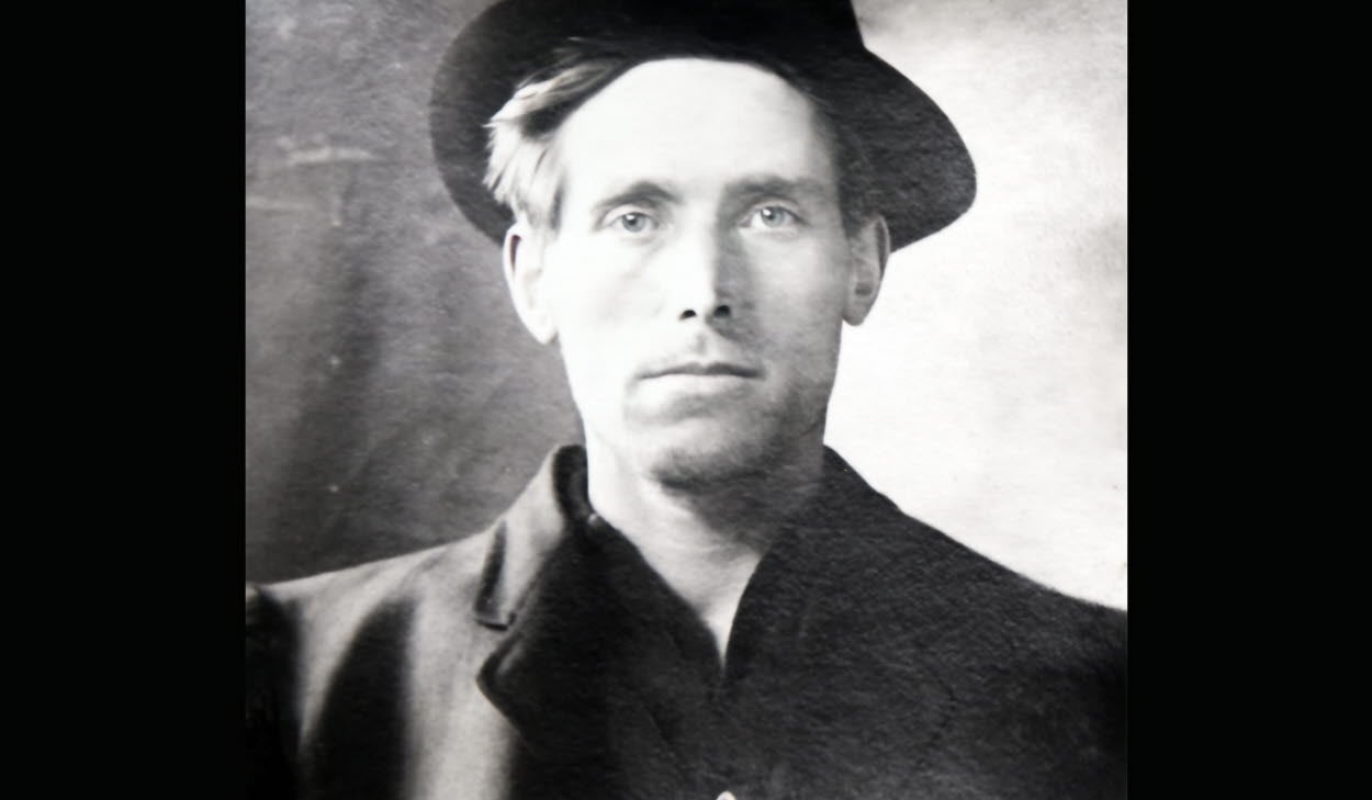Svartvit bild av författare Joe Hill iklädd rock och hatt. 