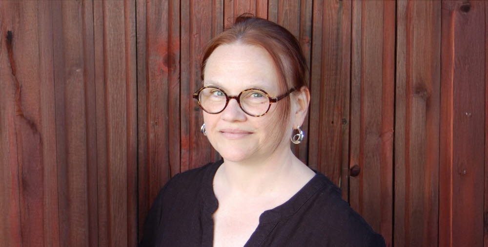 Porträtt av en person mot en träpanel i bakgrunden.