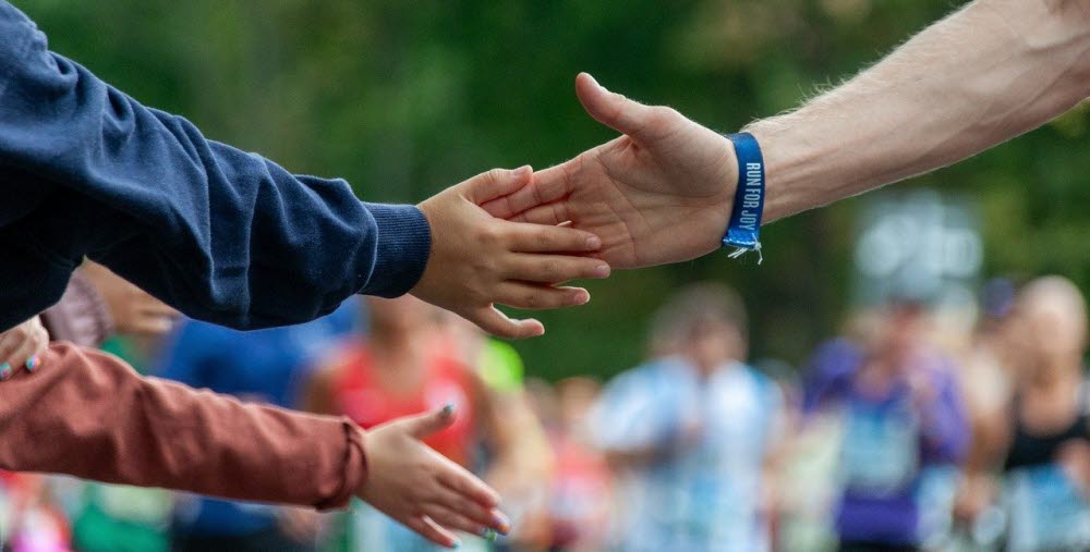 Händer som möts. I bakgrunden syns färgklädda människor.